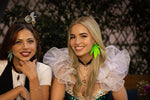Two women sitting at a table with a teapot and books, wearing decorative headbands.